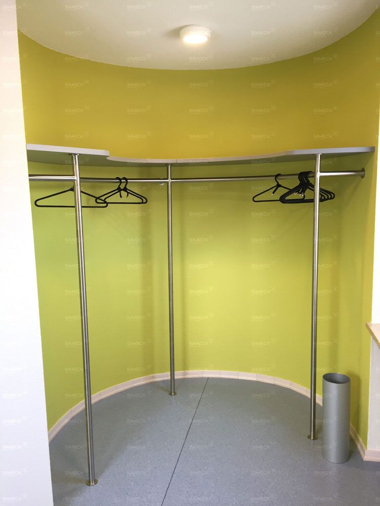 Ein Schrank mit einer gelben Wand und an Kleiderstangen hängender Kleidung.