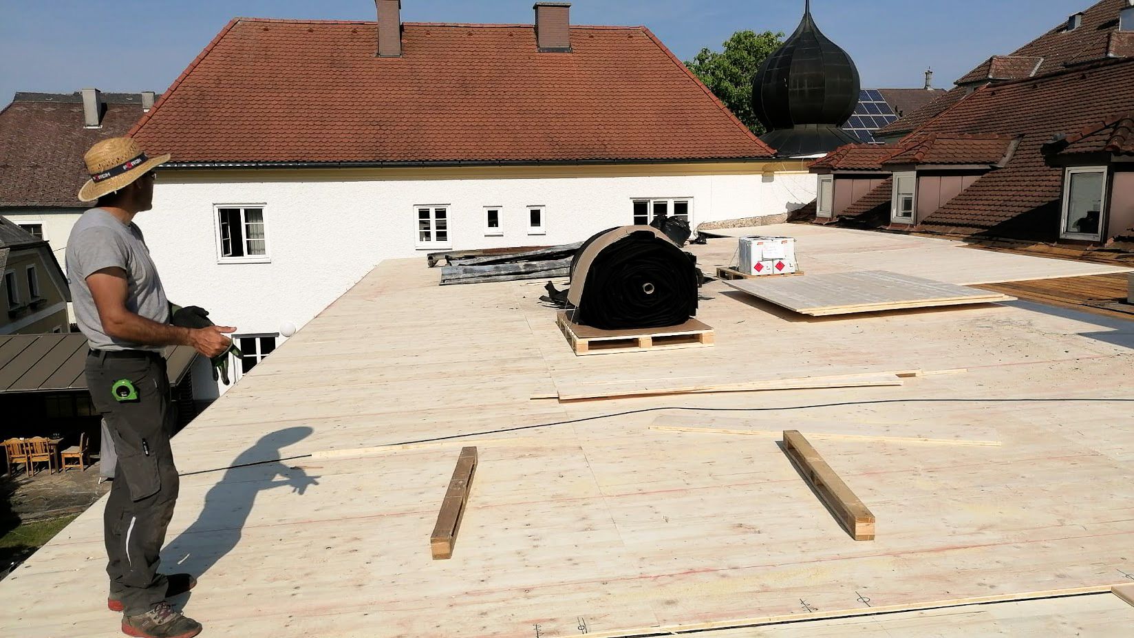 Ein Mann mit Strohhut steht auf einem Holzdach