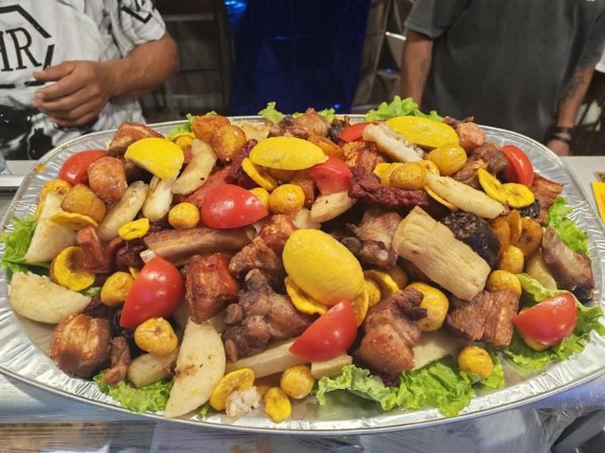 Gran fuente de carnes y verduras a la parrilla, adornada con rodajas de limón y tomates cherry, en una mesa de banquete.