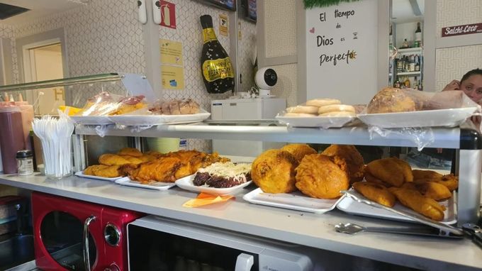 Mostrador de charcutería con pasteles variados y aperitivos fritos bajo una vitrina de cristal.