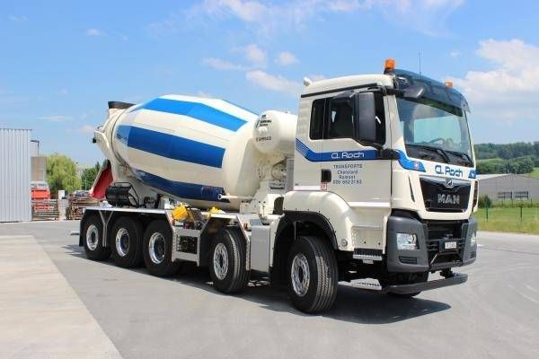 Camion malaxeur à béton blanc et bleu stationné sur un terrain pavé sous un ciel dégagé