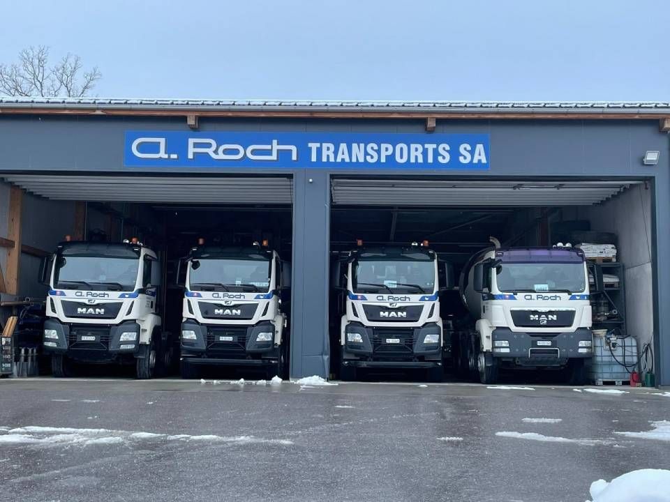Quatre tracteurs routiers blancs sont stationnés dans un garage chez CL Roch Transports SA.