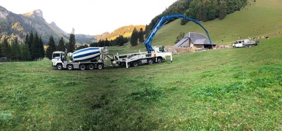Déversement de béton par camion et pompe à béton sur un chantier rural à flanc de colline verdoyante.