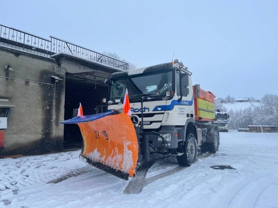 Un camion chasse-neige orange dégage une route enneigée près d'un pont en béton en hiver