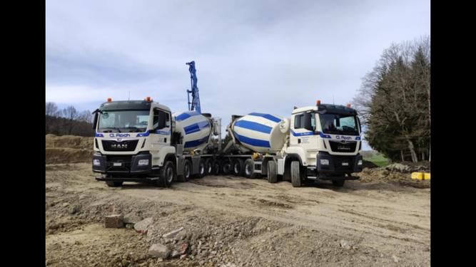 Camion grumier avec grue chargeant du bois coupé dans une cour en terre sous un ciel bleu clair