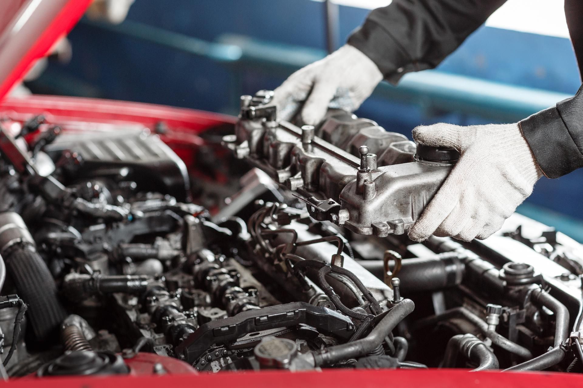 Ein Mechaniker mit Handschuhen arbeitet in einer Garage an einem offenen Automotor.