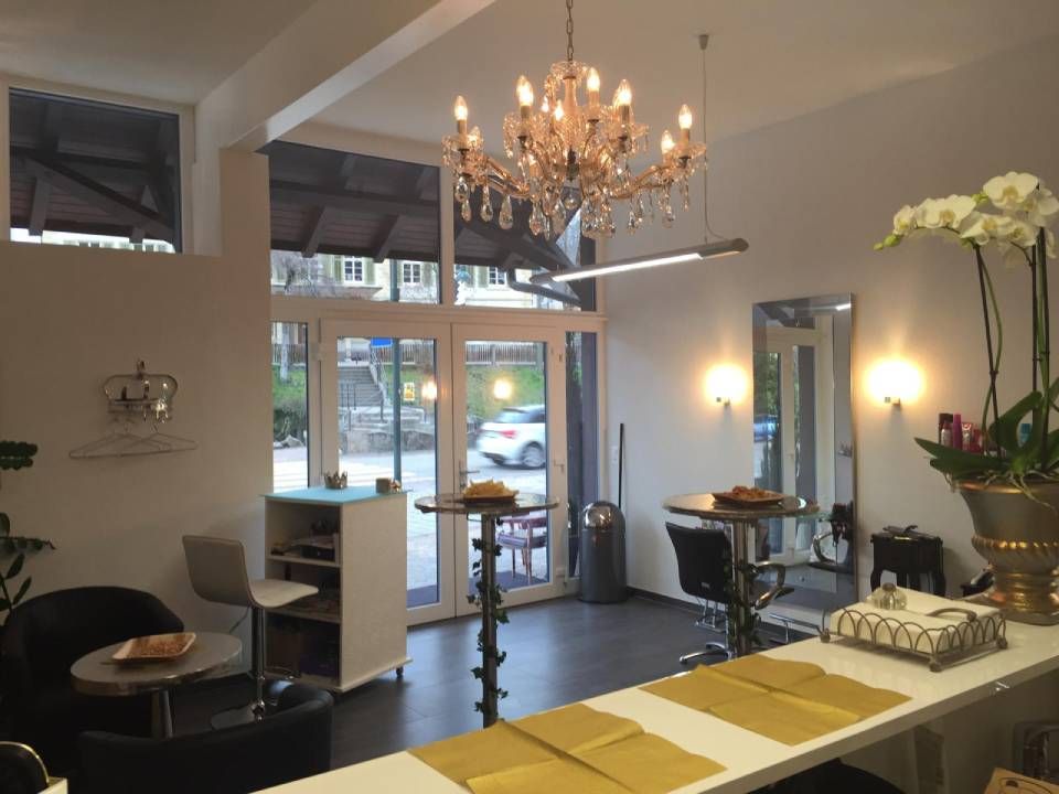 Hell erleuchteter Friseursalon mit Kristalllüster, modernen Frisierplätzen, Stühlen und weissen Wänden.