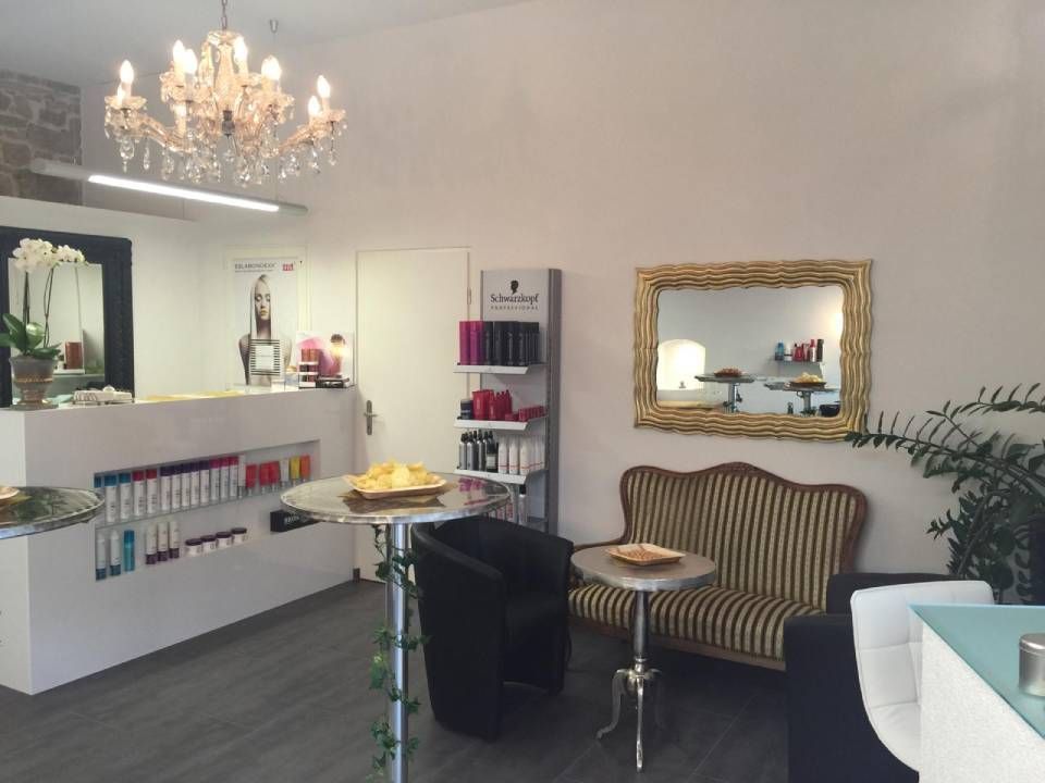 Das Interieur eines Friseursalons mit Kristalllüster, Empfangstresen, gestreiftem Sofa und Wandspiegel.