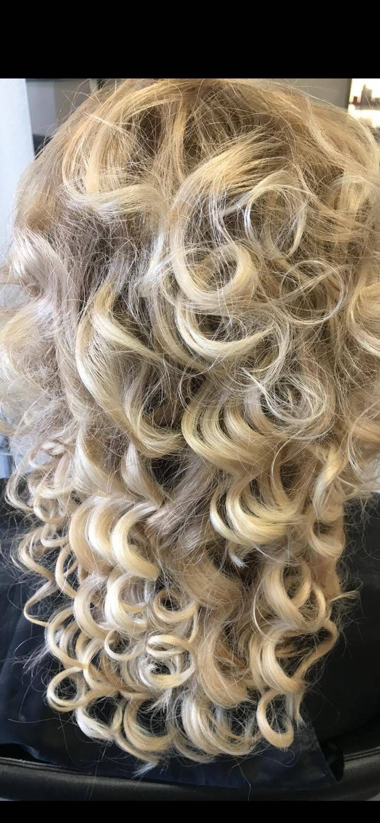 Langes, gestuftes blondes Haar, das zu engen, gleichmässigen Ringellocken frisiert ist.