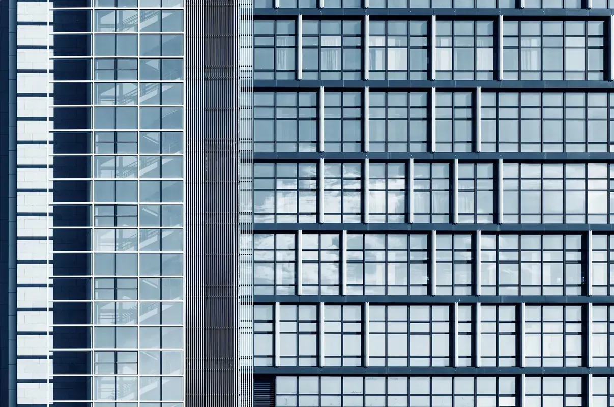 Modernes gläsernes Hochhaus mit gitterartigen Fenstermustern und einer schattigen Fassade, die den Himmel reflektiert.