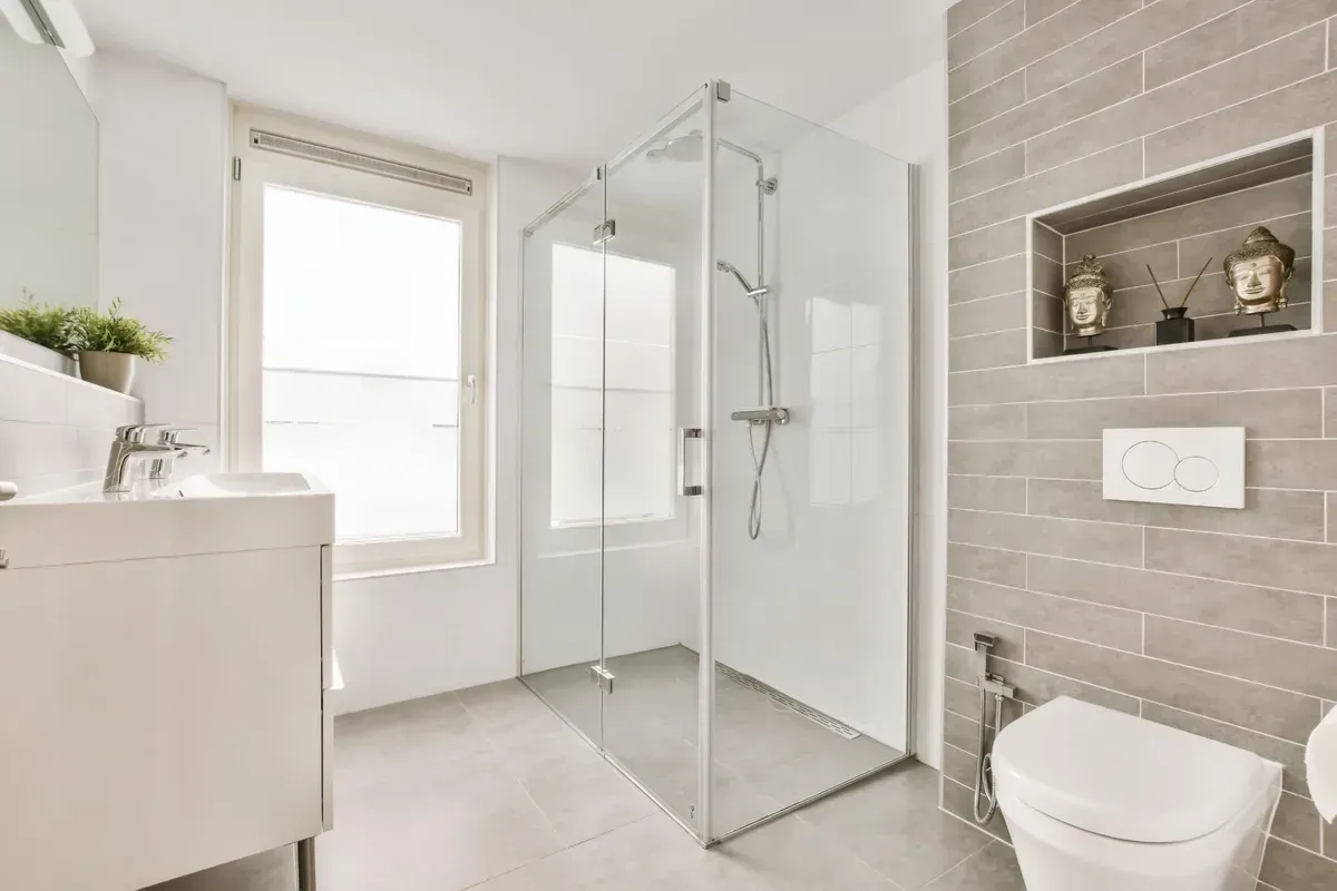 Modernes Badezimmer mit Glasdusche, grau gefliester Wand, Toilette und Waschbecken.