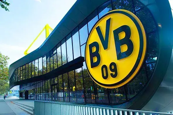 BVB Logo prangt auf einer modernen Gebäudefassade mit reflektierender Glasverkleidung. Farbgebung in Gelb und Schwarz.