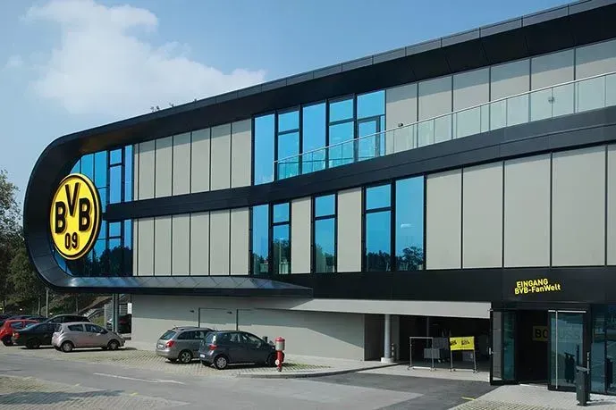 Modernes Gebäude mit großem „BVB“-Logo und getönten Fenstern; mehrere geparkte Autos.
