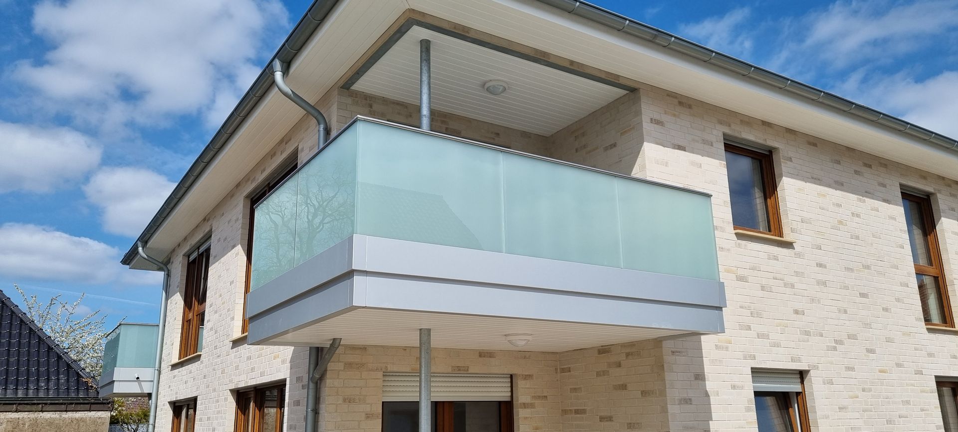 modernes Gebäude Ein modernes Gebäude mit Balkon. Der Balkon hat ein Geländer aus Glas und Metall und wird von Säulen getragen. Strahlend blauer Himmel.