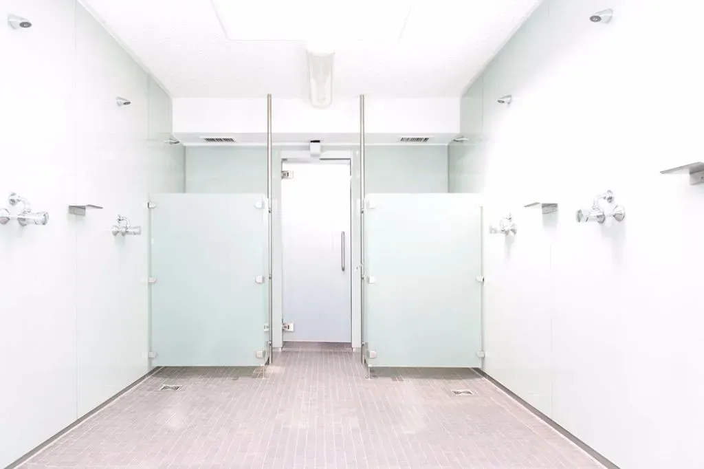 Ein heller, gefliester öffentlicher Duschraum mit Milchglas-Kabinentüren und silberfarbenen Armaturen.