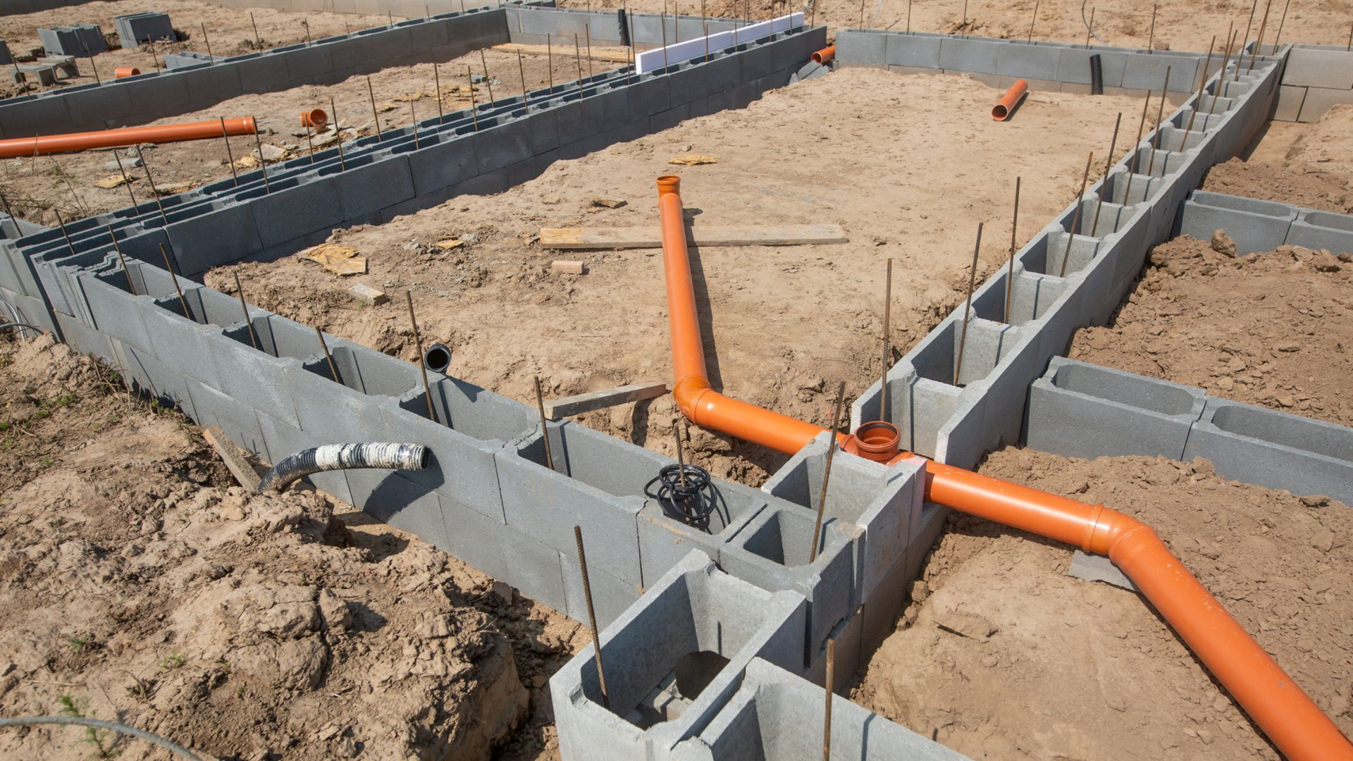 Fondations d'un bâtiment en construction, en blocs de béton, avec des tuyaux orange pour la plomberie.