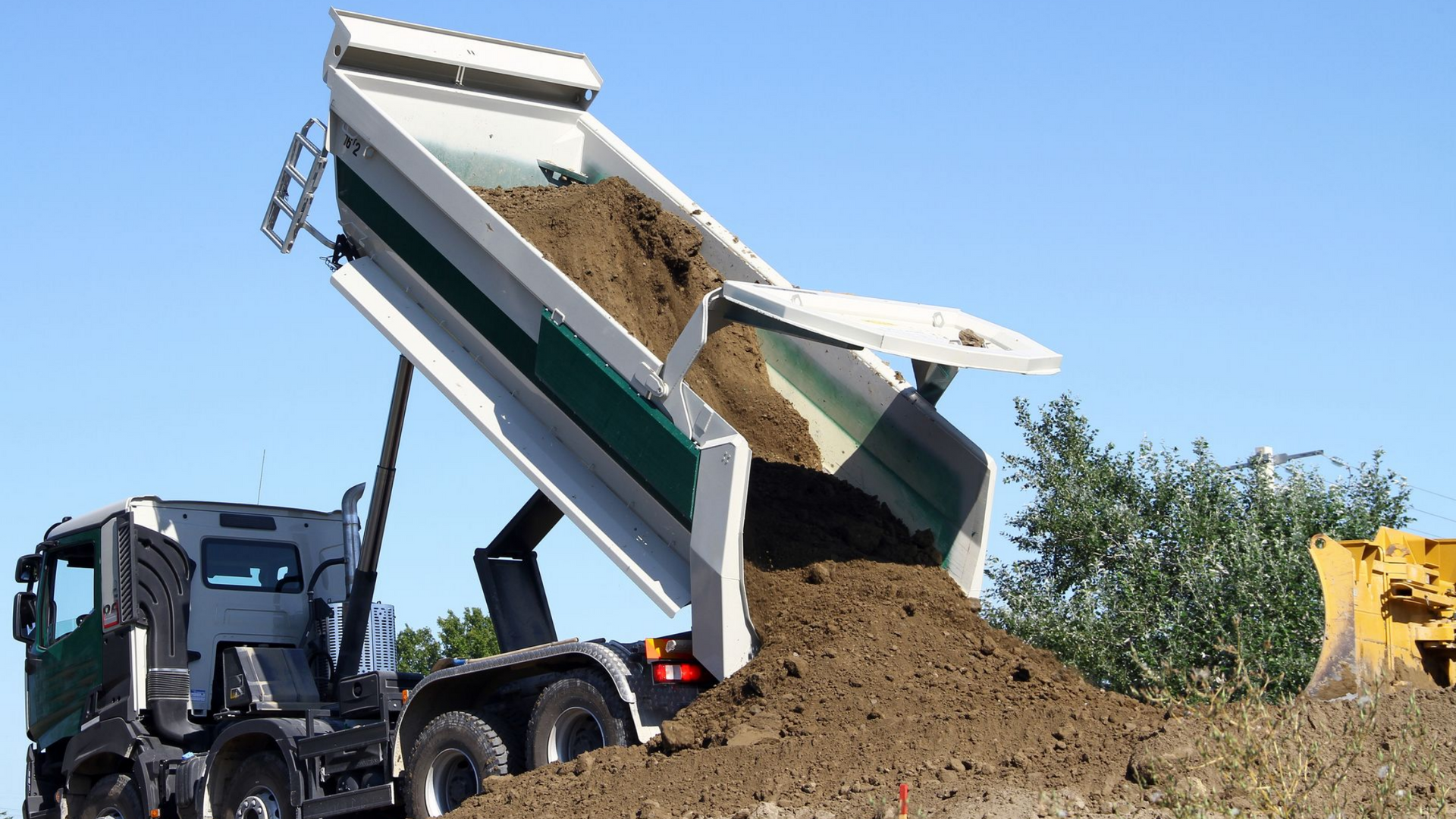 Un camion-benne déverse de la terre en plein air sous un ciel bleu.