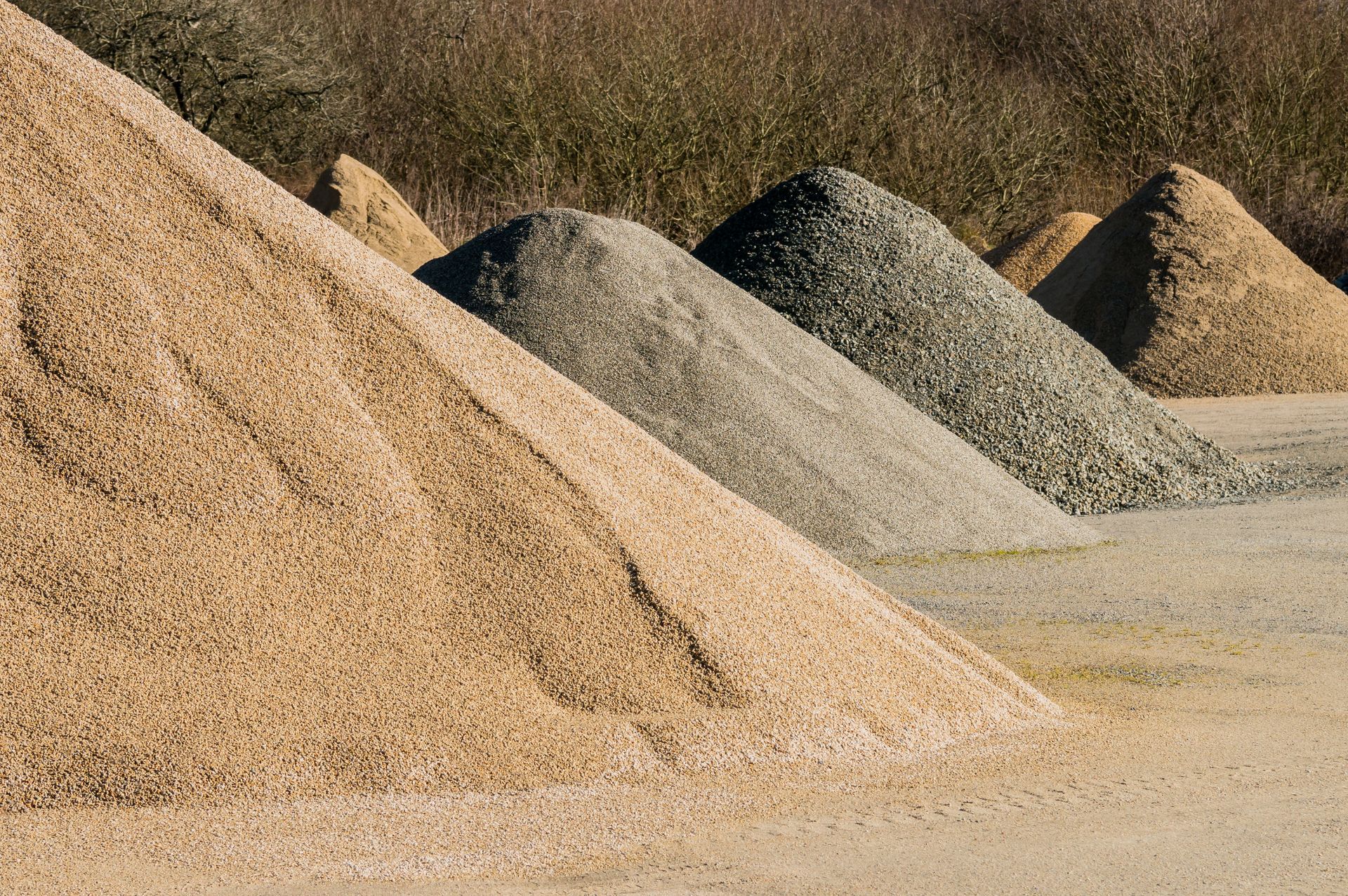 Des tas de gravier de différentes couleurs : beige, gris et vert. En extérieur, avec du feuillage brun en arrière-plan.