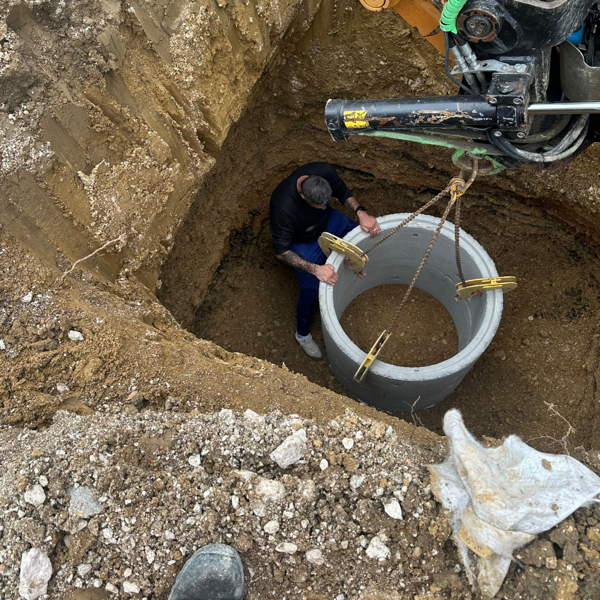 Un homme dans un trou guide un anneau de béton descendu par une machinerie.