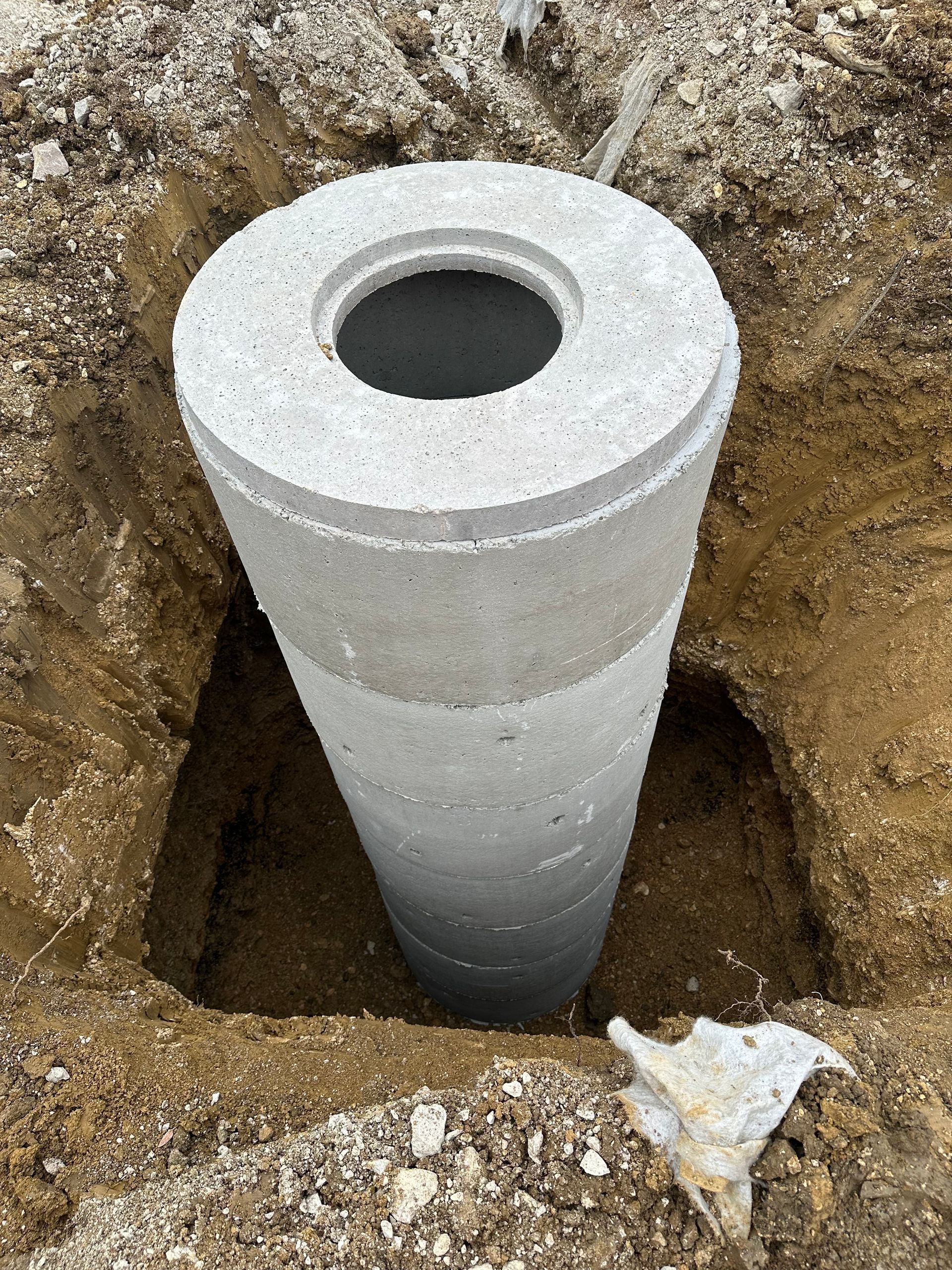 Cylindre de béton installé dans un trou creusé dans le sol, probablement un point d'accès aux services publics.