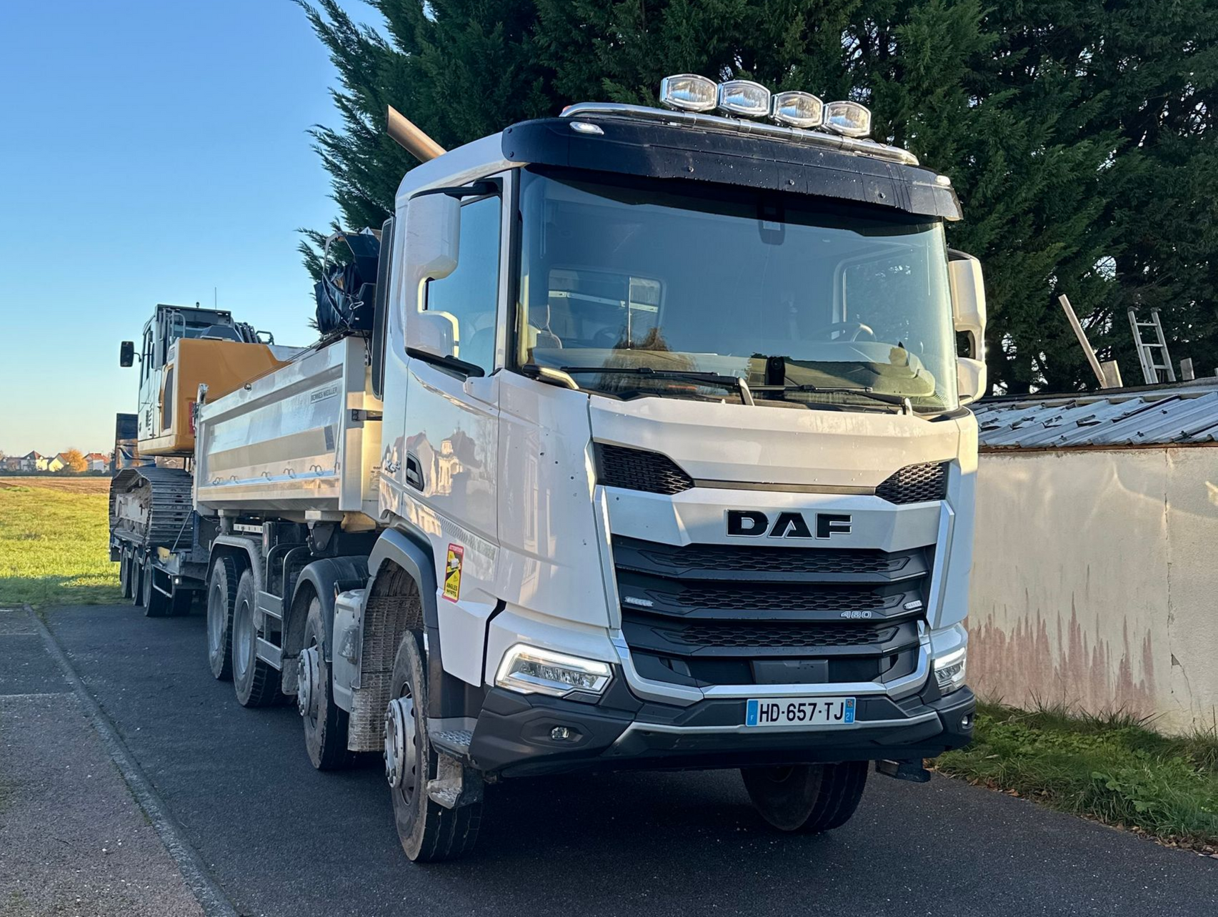 Un camion DAF blanc à benne basculante transporte du matériel de construction sur une route goudronnée.