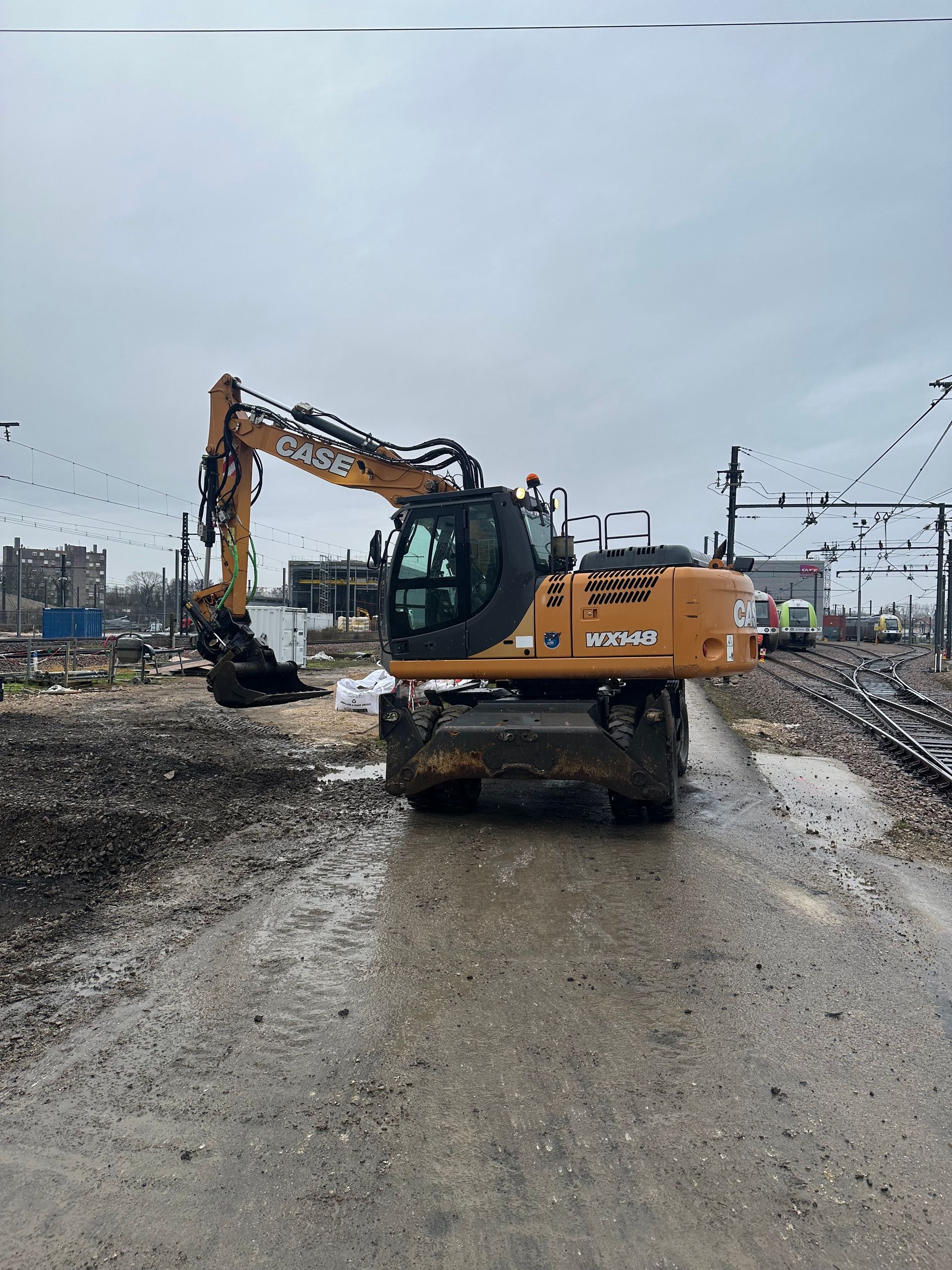 Une pelle mécanique Case sur un chantier boueux sous un ciel nuageux.