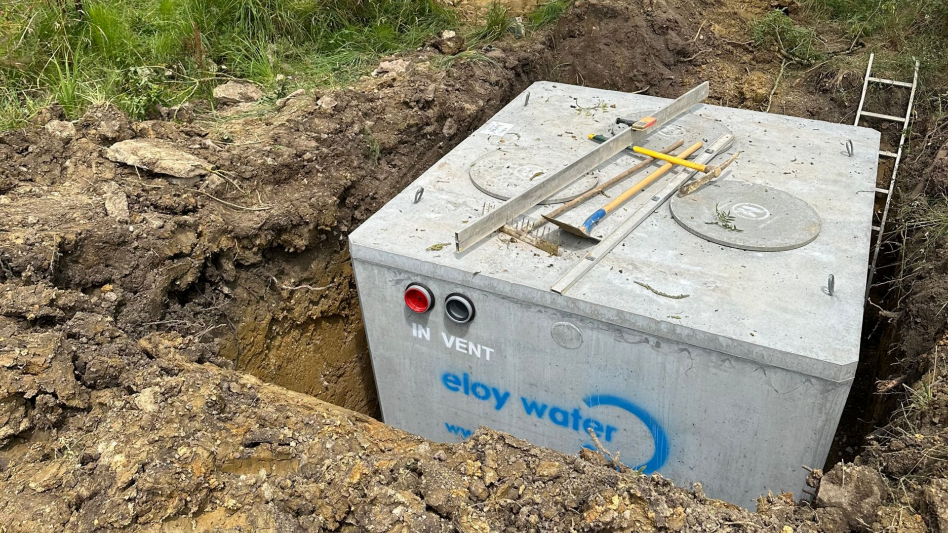 Réservoir d'eau en béton dans une fosse creusée, avec les outils sur le dessus, prêt à être installé.