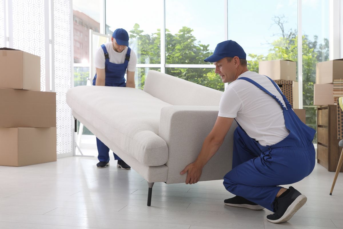 Zwei Männer verschieben ein weißes Sofa in einem Wohnzimmer.