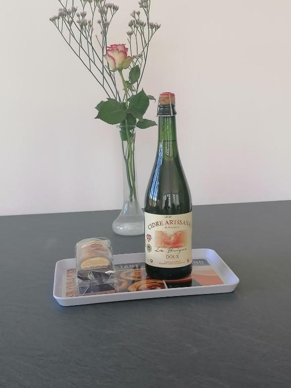 Bouteille de cidre sur un plateau avec un verre et un vase de fleurs sur une table.