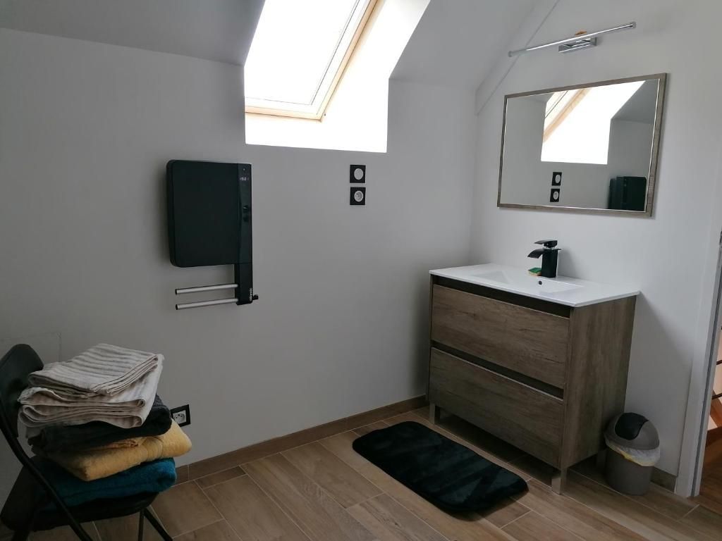 Salle de bains avec meuble-lavabo, miroir et serviettes. Tapis et chaise noirs. Parquet et murs en bois clair.
