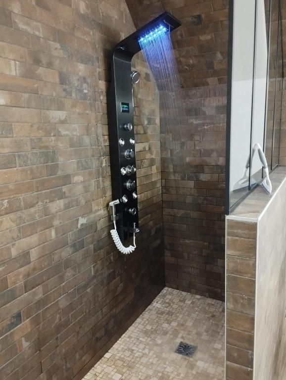 Un panneau de douche noir et chromé avec des lumières LED bleues sur fond de murs en briques marron.