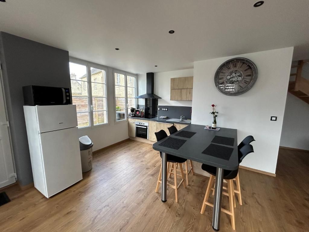 Cuisine moderne avec parquet en bois clair, murs gris, table noire et chaises en acier inoxydable.