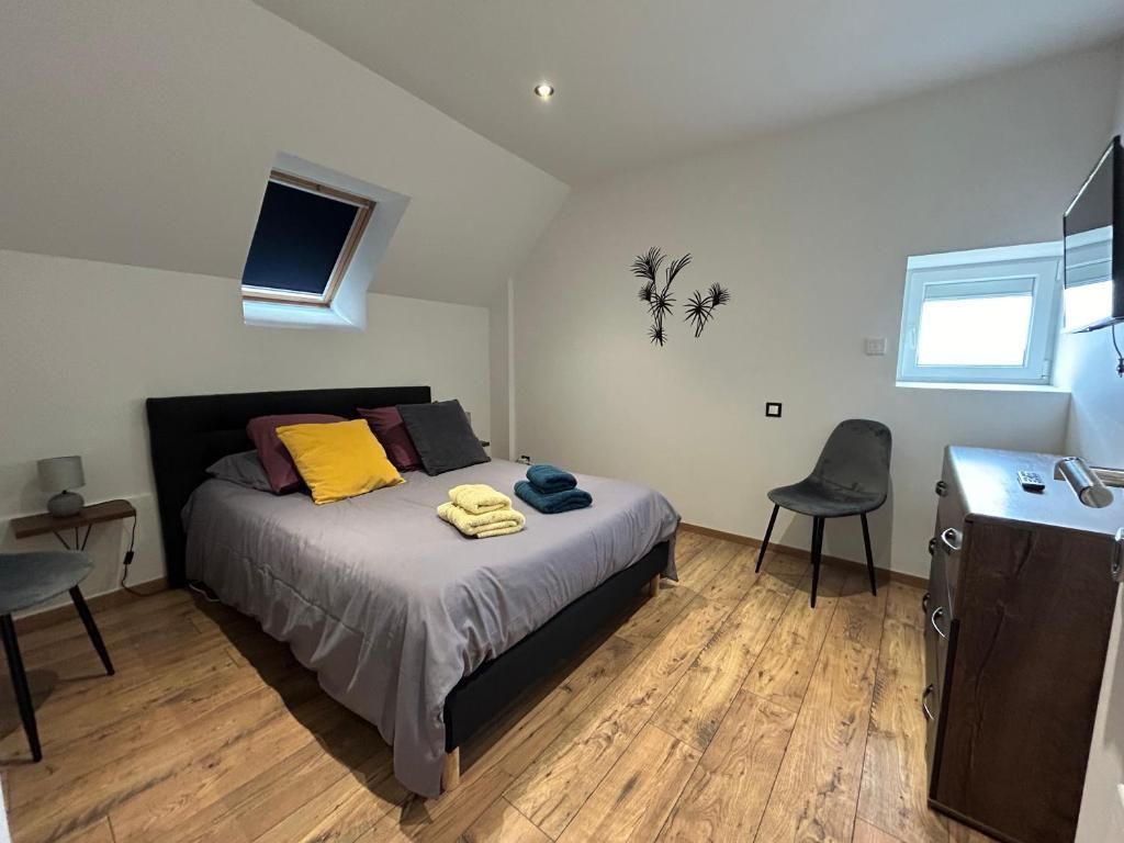 Chambre avec un lit double, parquet, petite fenêtre et chaise grise.