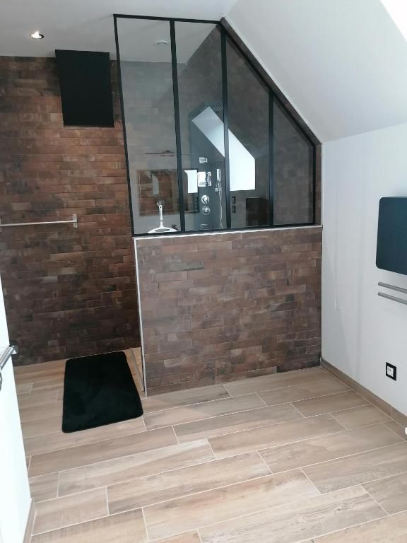 Salle de bains avec carrelage mural imitation brique, cabine de douche en verre, carrelage au sol imitation bois et tapis de bain noir.