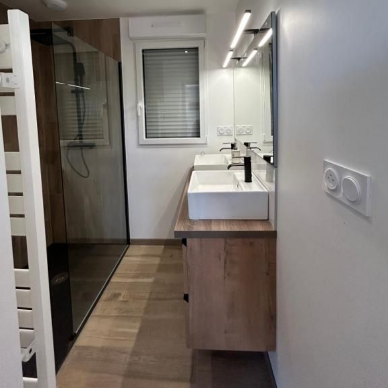 Salle de bains moderne avec deux lavabos, douche et accents en bois.