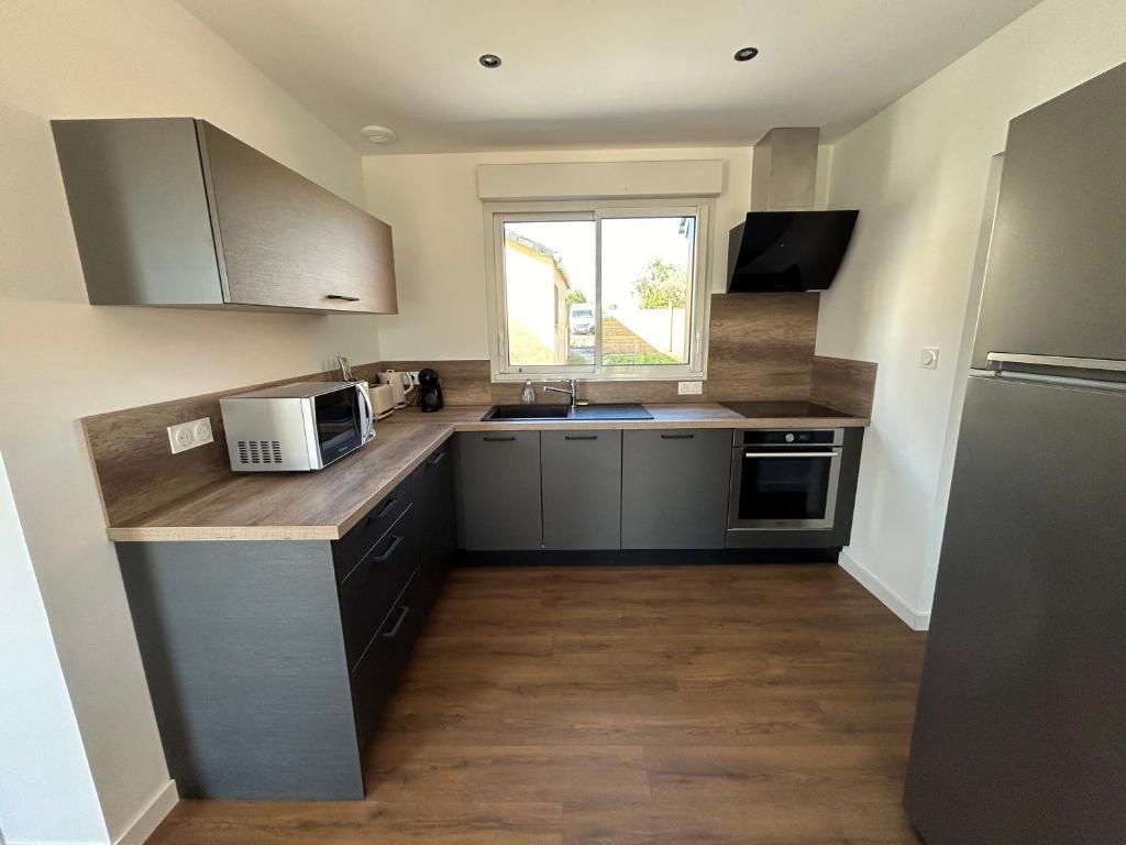 Cuisine grise moderne avec comptoirs en bois, appareils électroménagers en acier inoxydable et fenêtre.