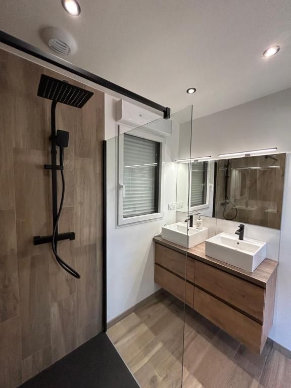 Salle de bains moderne avec sol imitation bois, pommeau de douche noir et double vasque avec deux lavabos blancs.