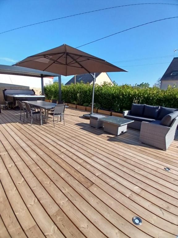 Terrasse en bois avec sièges extérieurs, table à manger et parasol sous un ciel ensoleillé.