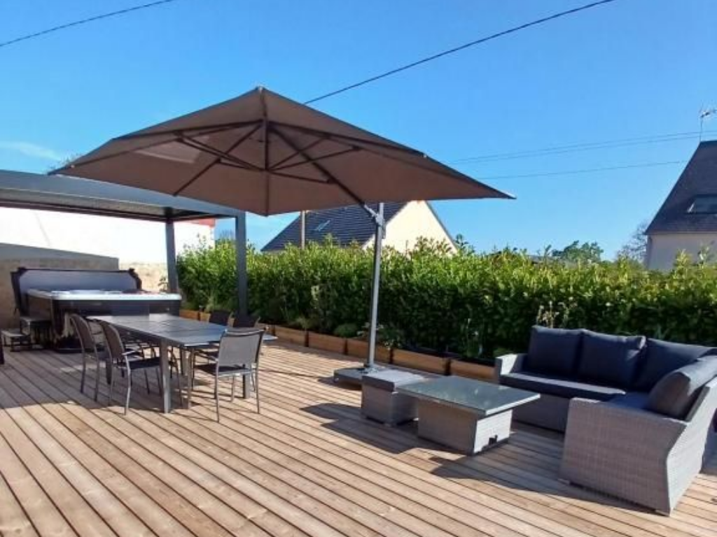 Patio extérieur avec terrasse en bois, ensemble de salle à manger, mobilier de salon, grand parasol et bain à remous.