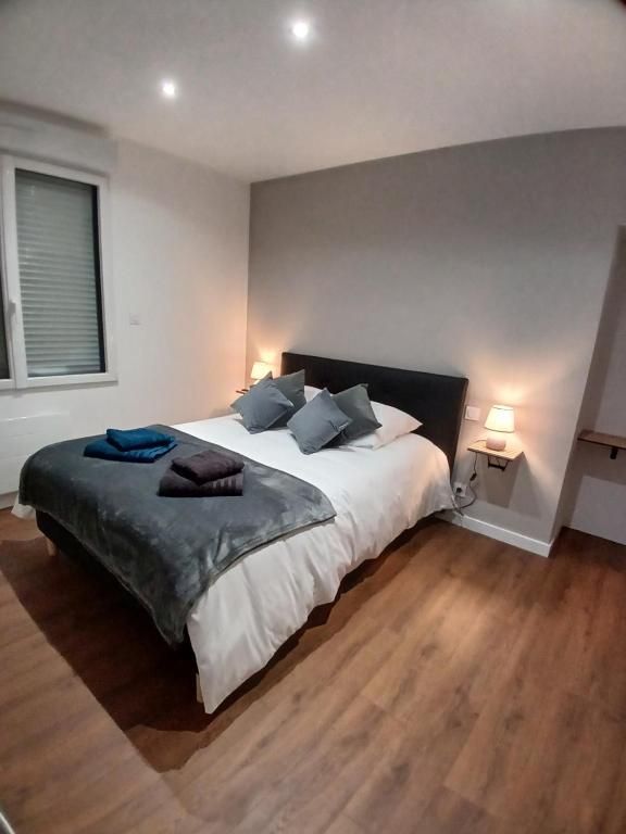 Chambre avec un lit, murs gris et parquet. Le lit est doté d'une couverture et d'oreillers gris. Il y a une fenêtre et des lampes.