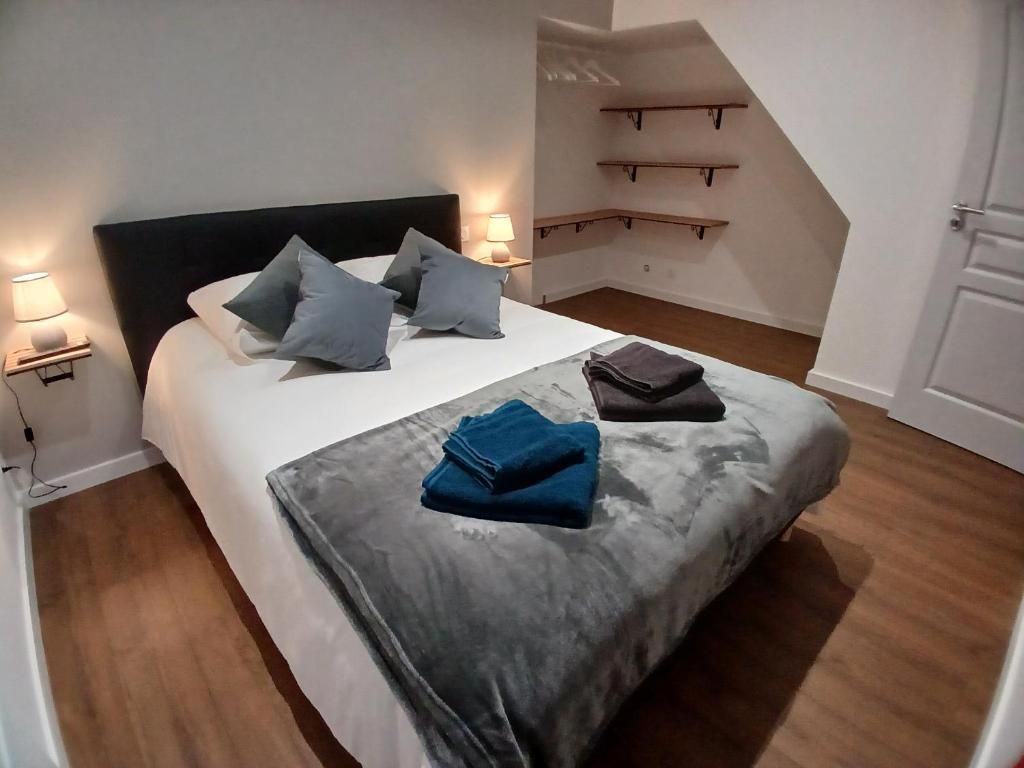 Chambre avec lit, oreillers, couvertures et parquet. Des étagères murales sont également présentes.