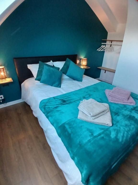 Chambre au mur turquoise, lit avec draps blancs, couverture et oreillers turquoise. Parquet.