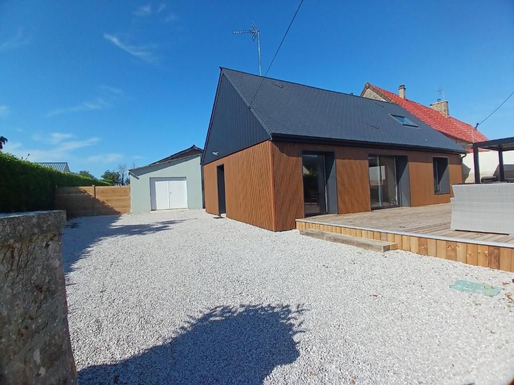 Maison moderne avec revêtement marron, toit gris et allée en gravier sous un ciel bleu.