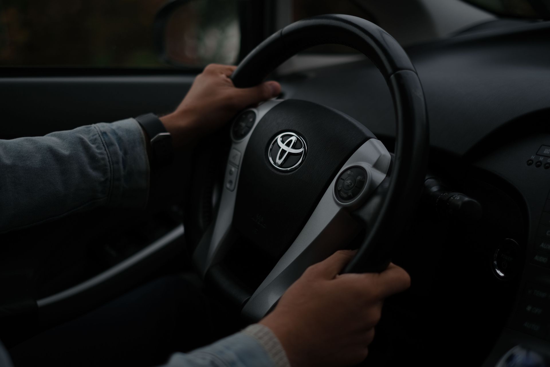 Manos agarrando el volante de un Toyota en el interior oscuro de un coche.