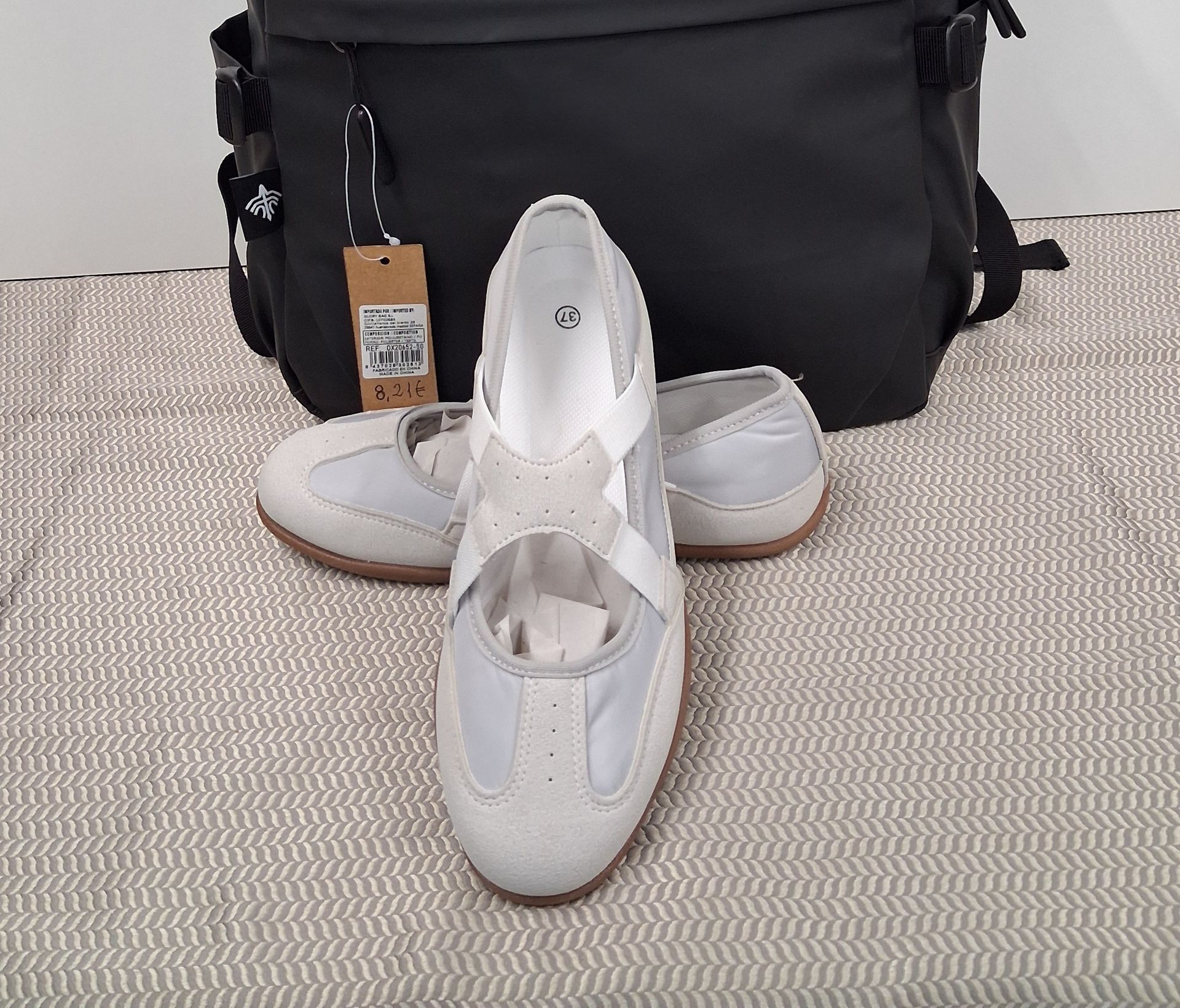 Zapatos blancos sin cordones delante de un bolso negro sobre una superficie texturizada.