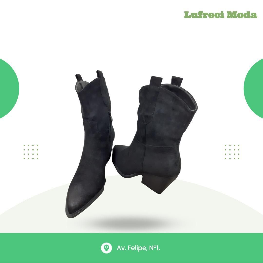 Un par de botas estilo vaquero de gamuza negra flotando sobre un fondo blanco con bordes verdes y la marca de la tienda.