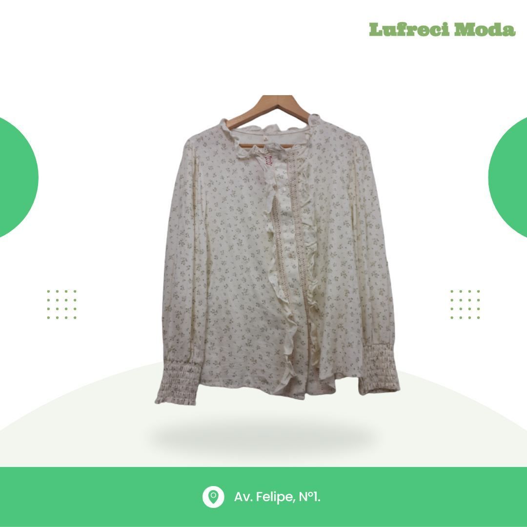 Blusa blanca con delicado estampado floral, volantes y mangas con puños, que cuelga sobre un fondo de la marca Lufreci Moda.