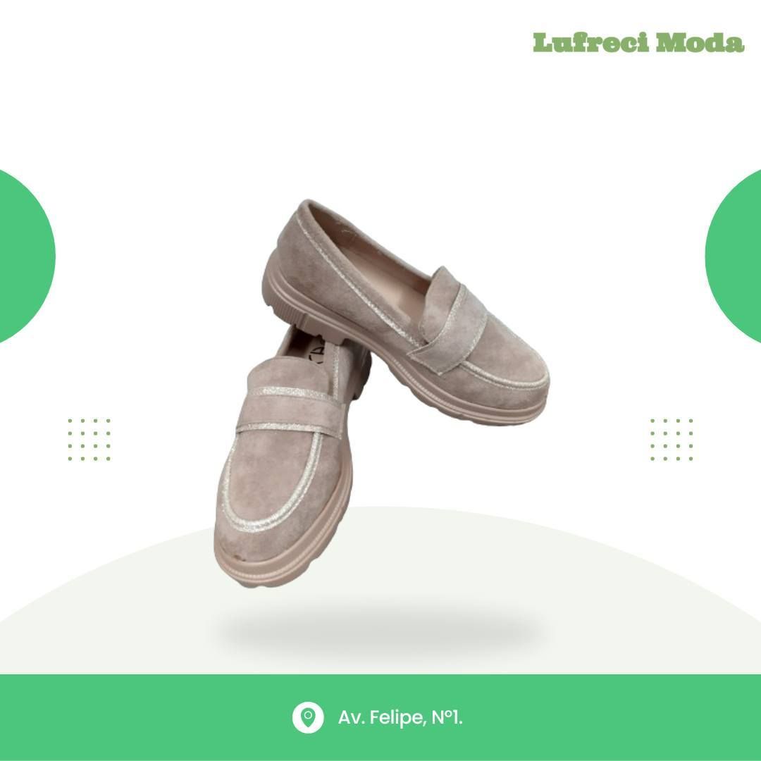 Un par de mocasines de gamuza beige sobre un fondo blanco con detalles verdes y el nombre de la tienda 