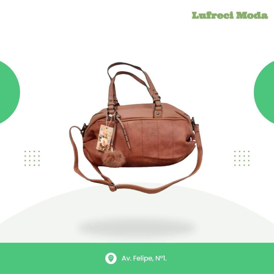 Bolso de mano marrón con bandolera y pequeño charm de pompón sobre fondo blanco con bordes verdes y detalles de tienda.