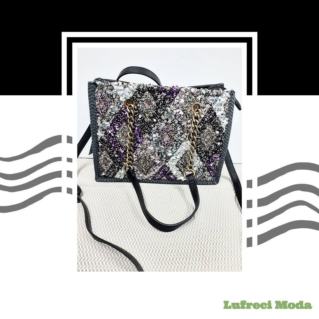 Un bolso negro estructurado con un patrón texturizado y brillante y detalles de cadena dorada, sobre un fondo liso.